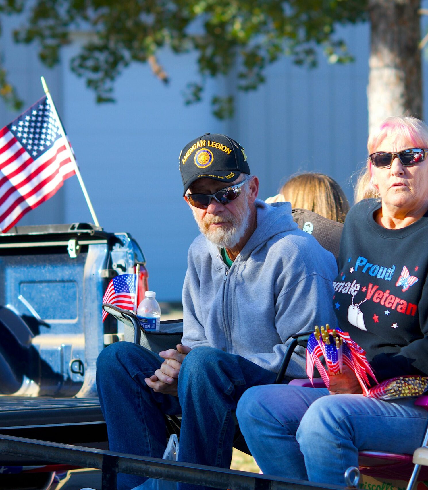 Senior veteran couple in a parade setting with American flags, showcasing patriotism and community spirit.